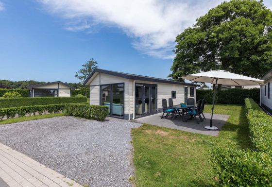 Vue sur le chalet Velthorst avec jardin, terrasse et parasol à EuroParcs Parc du Soleil aux Pays-Bas.