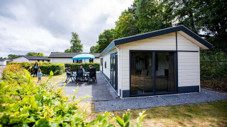 Vista esterna della cabina Comfort a EuroParcs Noordwijkse Duinen, con famiglia, patio e tanto verde.