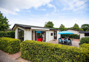 Feriehytte med terrasse og parasol hos EuroParcs Noordwijkse Duinen, Holland, tre personer udenfor.