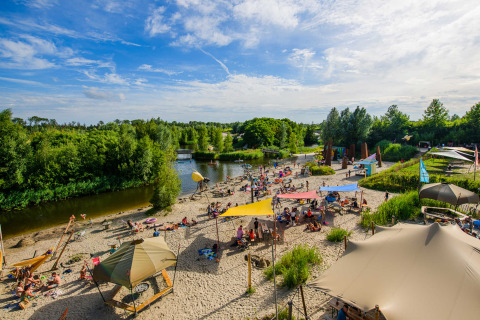 Strand aan Netl Camping Kallumaan vakantiepark in Flevoland, Nederland, met bezoekers en zonnetenten.