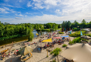 Strand aan Netl Camping Kallumaan vakantiepark in Flevoland, Nederland, met bezoekers en zonnetenten.