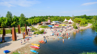 Escena de playa en Netl Camping Kallumaan en Flevoland, Holanda, con kayaks y familias disfrutando el agua.