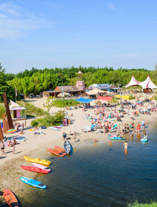 Escena de playa en Netl Camping Kallumaan en Flevoland, Holanda, con kayaks y familias disfrutando el agua.