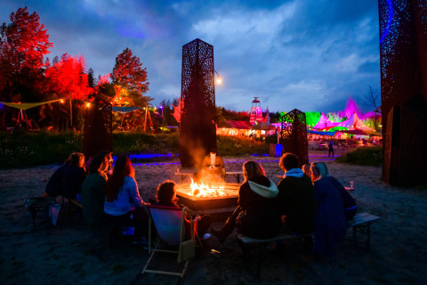 Un grupo de personas se sienta alrededor de una fogata en Netl Camping Kallumaan, Flevoland, Países Bajos, de noche.
