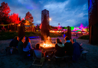 Un grupo de personas se sienta alrededor de una fogata en Netl Camping Kallumaan, Flevoland, Países Bajos, de noche.