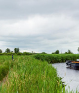 Paisaje cerca de Kallenkote, Overijssel, con canal, barcos, campos verdes y un molino de viento tradicional.
