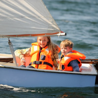 Dos niños con chalecos salvavidas navegan en un bote en el agua en un parque vacacional con glamping.