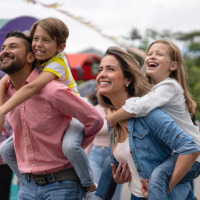 Familia feliz en un parque vacacional con glamping, padres dan paseos a caballito a sus hijos sonrientes.