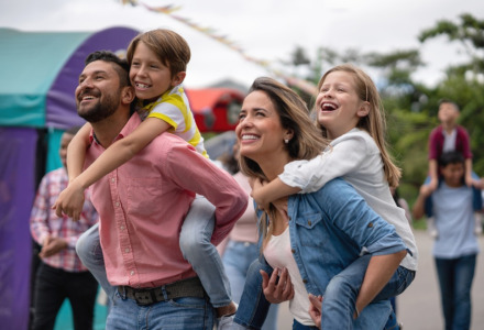 Familia feliz en un parque vacacional con glamping, padres dan paseos a caballito a sus hijos sonrientes.