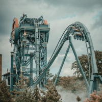 Foto de una gran montaña rusa en un parque vacacional con opciones de glamping, rodeado de árboles.