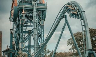Foto de una gran montaña rusa en un parque vacacional con opciones de glamping, rodeado de árboles.