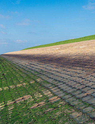 Dique cubierto de piedras y vegetación junto al mar cerca de Kamperland, Zelanda, Países Bajos y cielo azul.