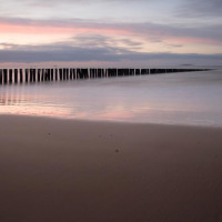 Tranquila playa cerca de Kamperland, Zelanda, Países Bajos, con postes de madera en el agua al atardecer.