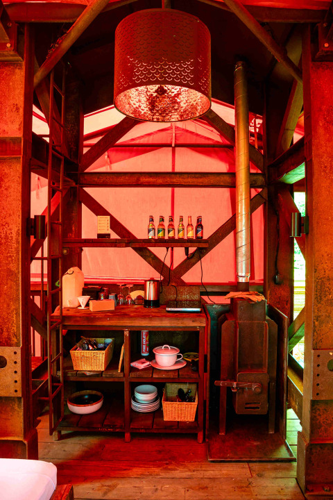 Cuisine rustique et poêle à bois dans la cabane BoomBoom à Netl Camping Kallumaan, Pays-Bas, lumière rouge.