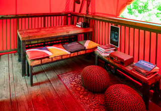 Intérieur de cabane dans les arbres avec banc, coussins colorés et mobilier en bois au Netl Camping Kallumaan.