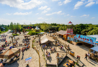 Solrig campingplads med telte, strand, farverige bygninger og mennesker, der nyder glamping-oplevelsen.