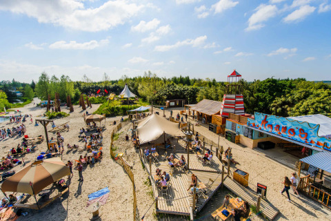 Alojamiento glamping soleado con tiendas, playa, terrazas y personas disfrutando actividades al aire libre.