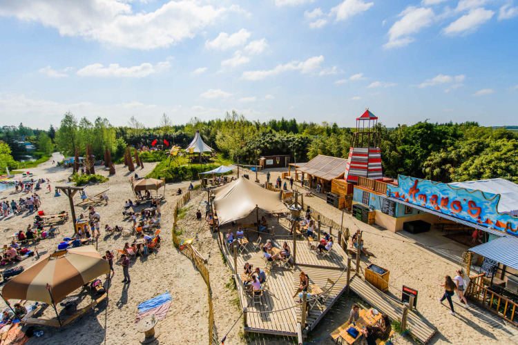 Alojamiento glamping soleado con tiendas, playa, terrazas y personas disfrutando actividades al aire libre.