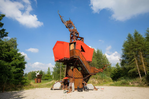 Alojamiento glamping único hecho de madera y lona roja, situado en la naturaleza bajo un cielo azul brillante.
