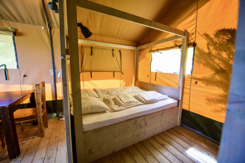 Vista interior de una tienda safari con cama de madera, mesa y sillas en Netl Camping Kallumaan, Países Bajos.