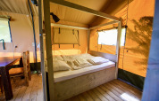 Interior view of a safari tent with a wooden bed, table, and chairs at Netl Camping Kallumaan, Netherlands.