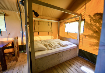 Vue intérieure d'une tente safari avec lit en bois, table et chaises au Netl Camping Kallumaan, Pays-Bas.