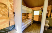 Interior de la tienda safari Lodge + sanitary Leri - UFO en Netl Camping Kallumaan, Países Bajos, con literas y baño.