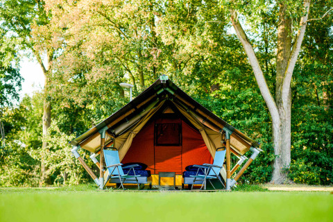 Tienda safari Lodge Mokki - UFO en un bosque verde, dos sillas azules delante, ambiente relajado.