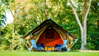 Safari tent Lodge Mokki - UFO in a green forest, two blue chairs in front, relaxing camping vibe.