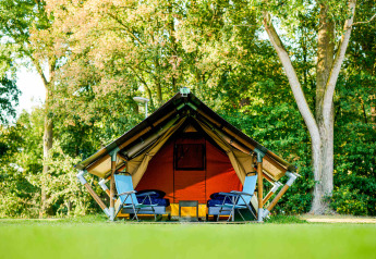 Tienda safari Lodge Mokki - UFO en un bosque verde, dos sillas azules delante, ambiente relajado.
