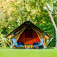 Tienda safari Lodge Mokki - UFO en un bosque verde, dos sillas azules delante, ambiente relajado.