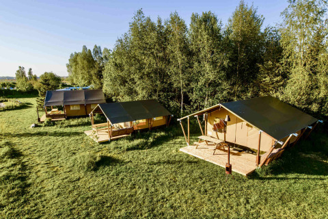 Photo of three safari tents set on a grassy field next to a forest, ideal for glamping and outdoor retreats.