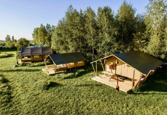 Photo of three safari tents set on a grassy field next to a forest, ideal for glamping and outdoor retreats.