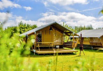 Sunny day at a glamping site featuring modern safari tents with a wooden deck set on a lush green field.