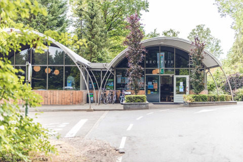 Entrada del parque vacacional Veluwepark de Bosgraaf en Gelderland, Países Bajos, con bicicletas y vegetación.
