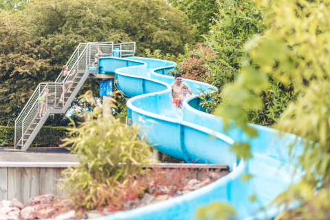 Familias disfrutan de un tobogán acuático azul rodeado de árboles en Veluwepark de Bosgraaf, Gelderland.