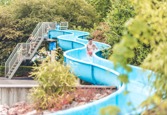 Familier nyder en blå vandrutsjebane omgivet af frodige træer i Veluwepark de Bosgraaf, Gelderland.