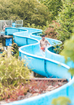 Familias disfrutan de un tobogán acuático azul rodeado de árboles en Veluwepark de Bosgraaf, Gelderland.