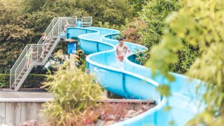 Familias disfrutan de un tobogán acuático azul rodeado de árboles en Veluwepark de Bosgraaf, Gelderland.