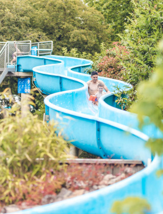 Familias disfrutan de un tobogán acuático azul rodeado de árboles en Veluwepark de Bosgraaf, Gelderland.