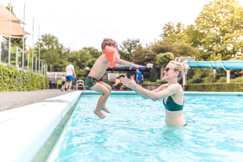 Niño salta a la piscina hacia un adulto en Veluwepark de Bosgraaf, parque vacacional en Gelderland, Países Bajos.