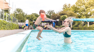 Niño salta a la piscina hacia un adulto en Veluwepark de Bosgraaf, parque vacacional en Gelderland, Países Bajos.