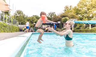 Niño salta a la piscina hacia un adulto en Veluwepark de Bosgraaf, parque vacacional en Gelderland, Países Bajos.