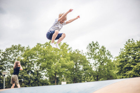 A child jumps high on a bouncy cushion at Veluwepark de Bosgraaf, surrounded by green trees in Gelderland.