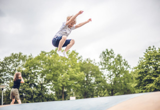 A child jumps high on a bouncy cushion at Veluwepark de Bosgraaf, surrounded by green trees in Gelderland.