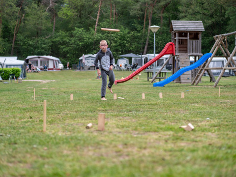 Boy playing kubb on grassy field at a holiday park with playground and caravans in Gelderland, Netherlands.
