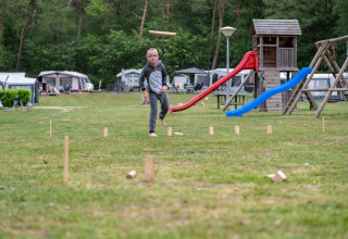 Boy playing kubb on grassy field at a holiday park with playground and caravans in Gelderland, Netherlands.
