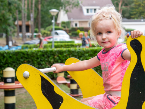 Kleines blondes Mädchen spielt auf einer gelben Wippe auf dem Spielplatz im Recreatiepark de Wrange, Gelderland.