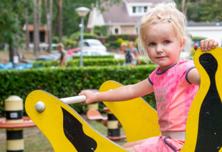 Kleines blondes Mädchen spielt auf einer gelben Wippe auf dem Spielplatz im Recreatiepark de Wrange, Gelderland.