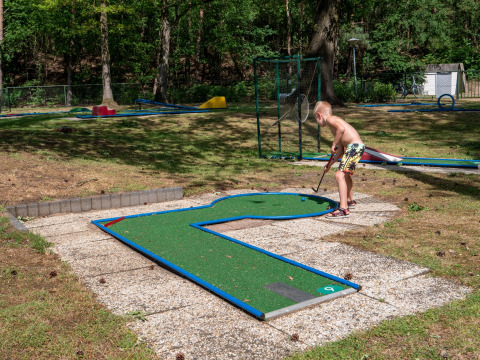 Boy playing mini golf at an outdoor course in sunlight at Recreatiepark de Wrange, Gelderland, Netherlands.